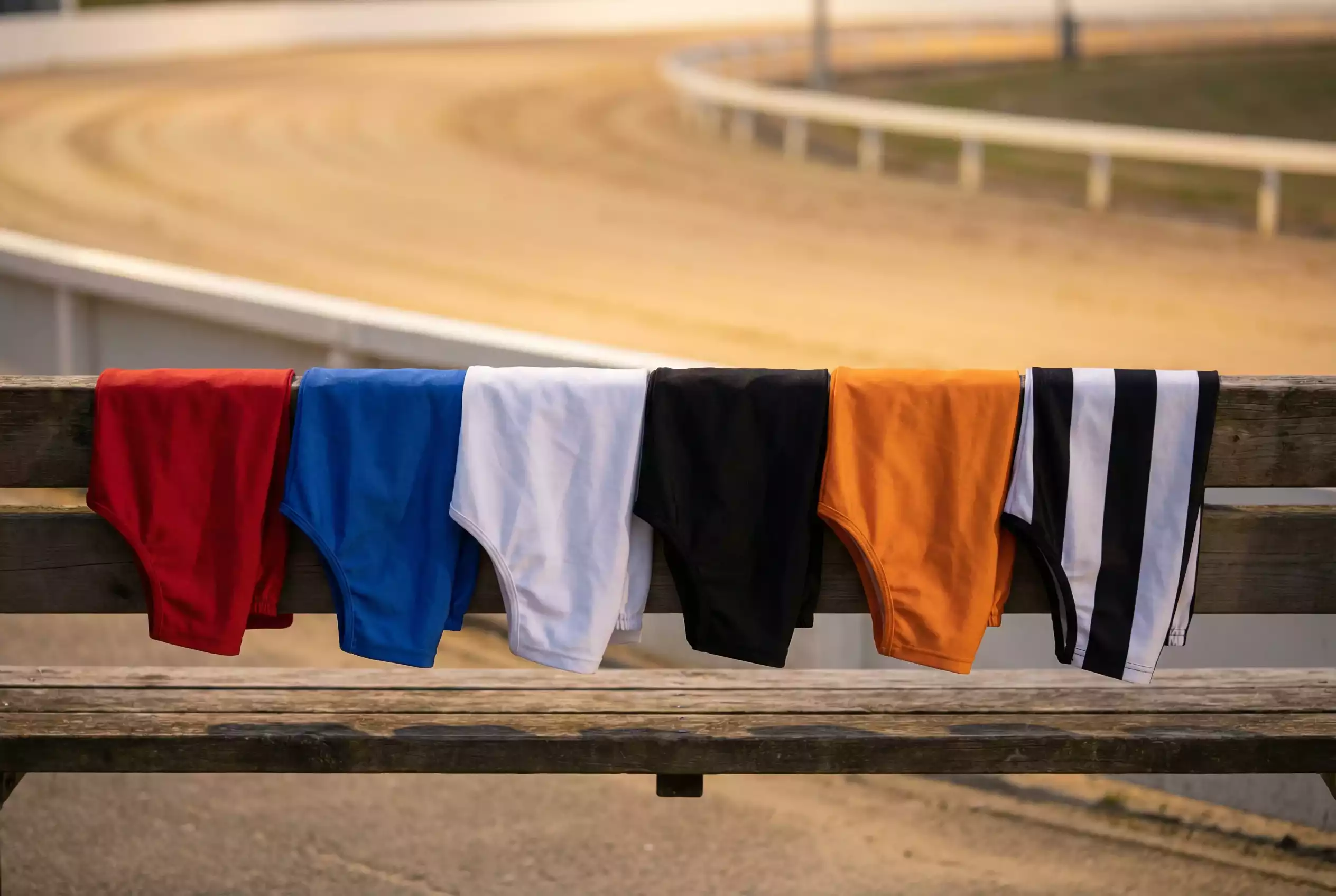 Six greyhound racing jacket colours lined up showing red, blue, white, black, orange and striped